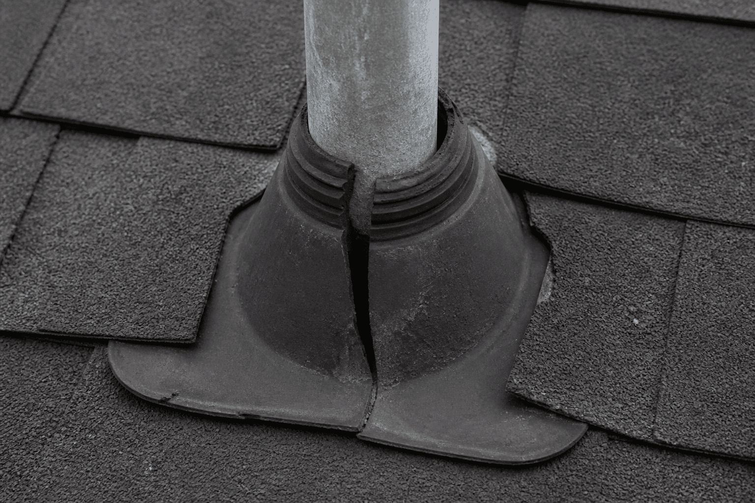 Plumbing vent on an asphalt roof with the black rubber boot cracked and split around the pipe