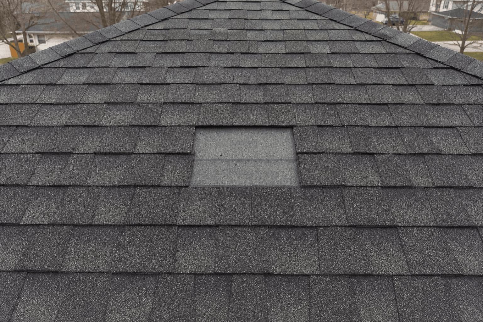 Charcoal architectural shingles with two tabs missing in the center, gray underlayment showing through the gap