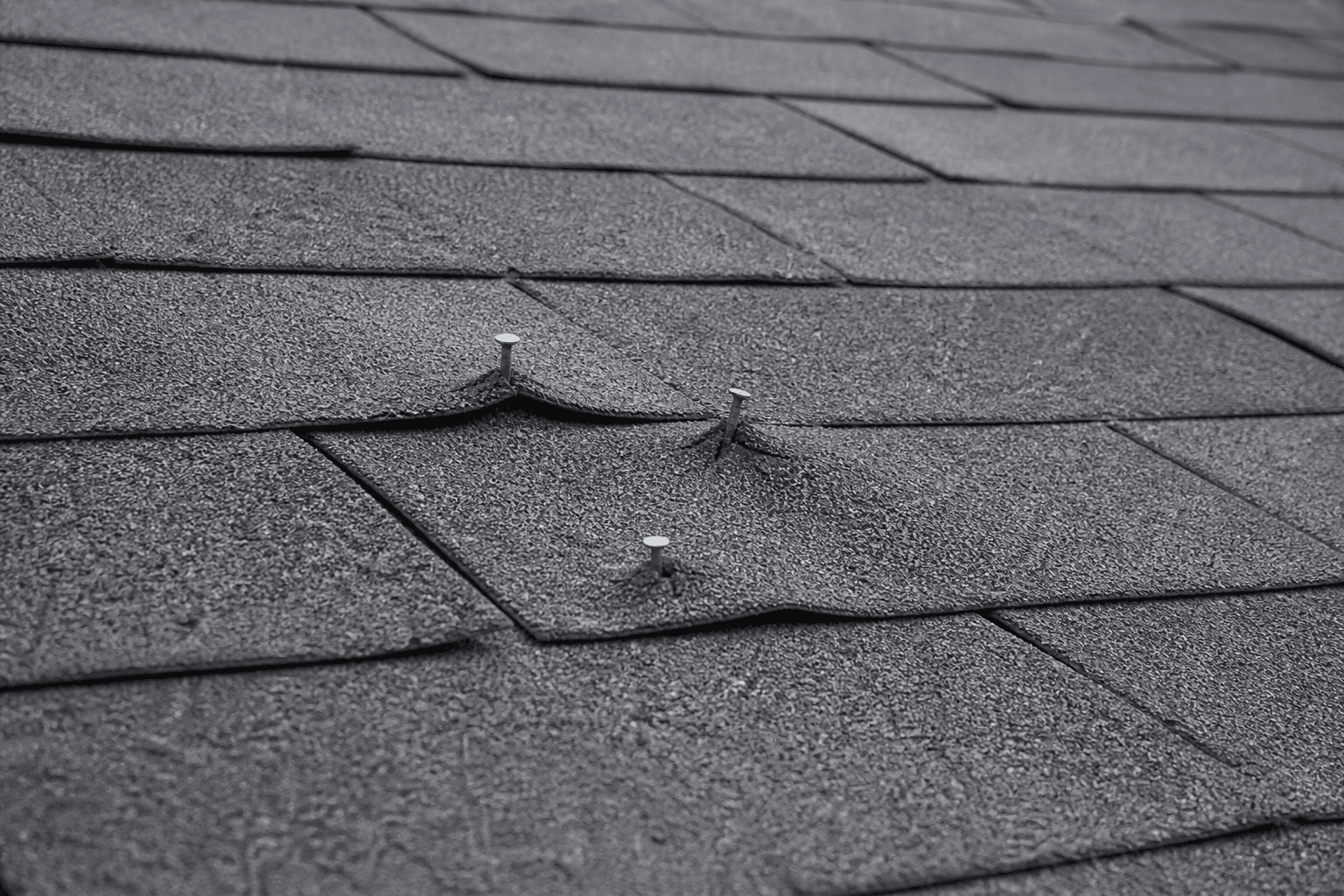 Close-up of charcoal shingles with nail heads popped through the tabs in the center of the field
