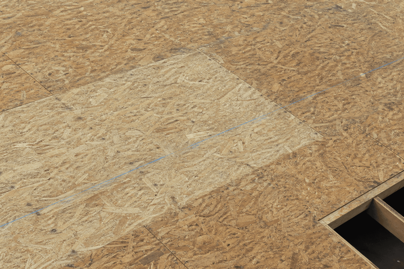 OSB roof deck: wood-flake sheets, seams, nails, a chalk line, and an open bay showing rafters