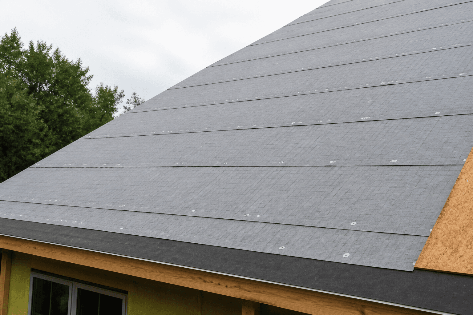 Gray synthetic underlayment with cap nails; black ice-and-water at the eave; OSB still visible at the edge